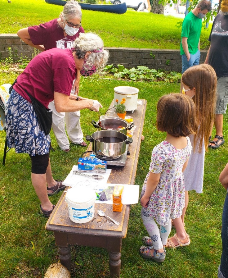 Children and volunteers at an outdoor table dyeing wool tassels with natural pigments.